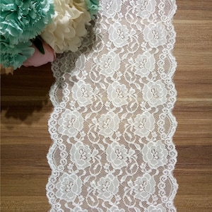 Könnte beinhalten: Weiße Spitzenborte mit Blumenmuster. Die Spitze ist zart und hat einen gewellten Rand.