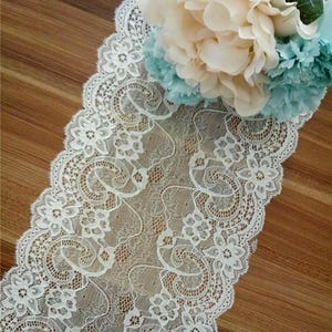 May include: White lace trim with a scalloped edge. The lace has a delicate floral pattern.