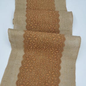 May include: A rolled-up burlap table runner with a decorative floral lace center. The lace is a warm brown color, and the burlap is a natural tan color. The runner is suitable for weddings, parties, or home decor.