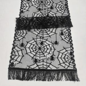 Könnte beinhalten: Schwarzer Spitzen-Tischläufer mit Spinnennetz- und Spinnen-Design. Der Läufer hat einen Fransenrand.