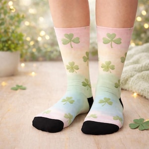 Puede incluir: Un par de calcetines hasta la rodilla con un degradado pastel de rosa, amarillo y azul. Los calcetines están decorados con patrones de tréboles verdes. Los dedos y los talones son negros.