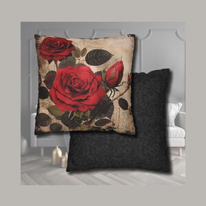 Puede incluir: Dos cojines decorativos. Uno presenta un diseño de rosas rojas grandes sobre un fondo de estilo vintage. El segundo cojín es negro liso con un sutil estampado floral. Los cojines son cuadrados y rectangulares.