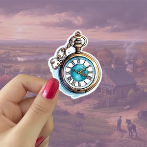May include: A gold pocket watch with a blue face and Roman numeral markings. The watch has a chain attached to it and is held in a hand against a blurred background of a rural landscape.