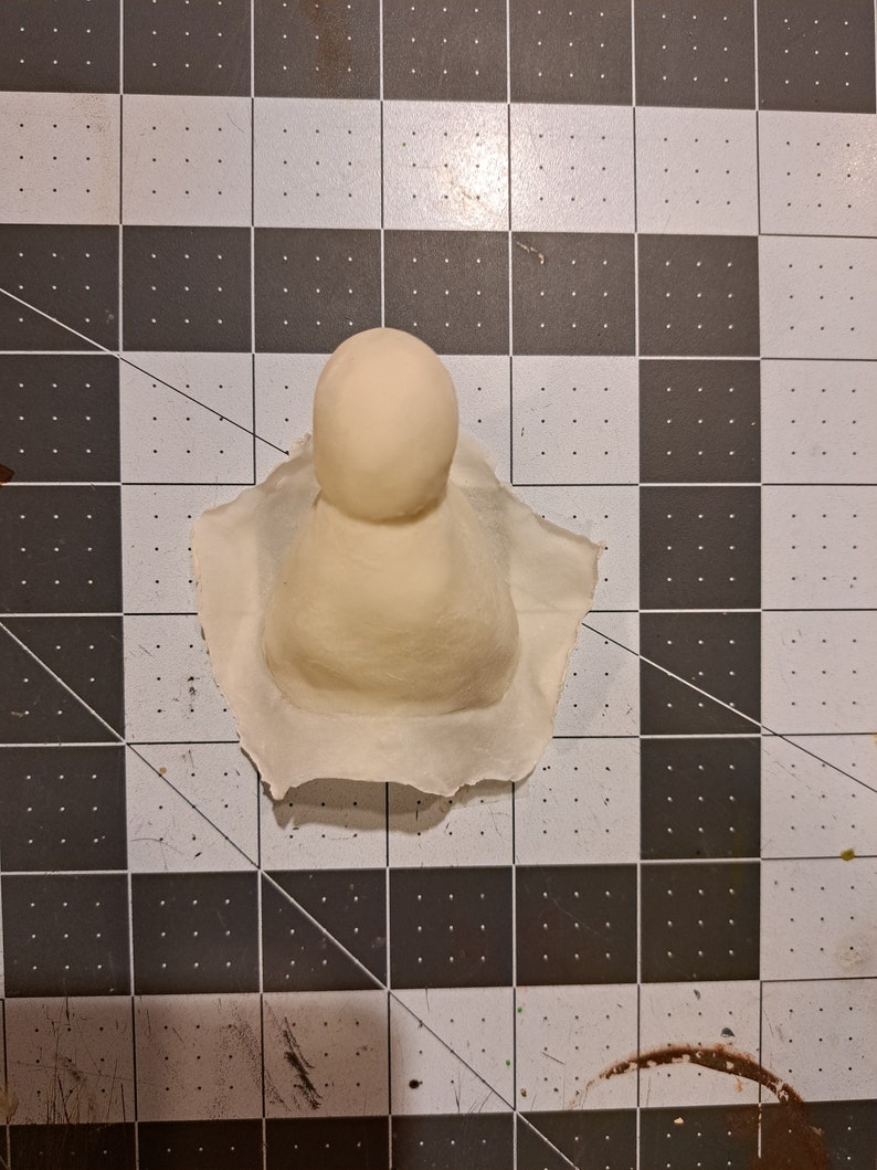 May include: A white clay sculpture of a person with a round head and a cone-shaped body.