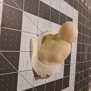 May include: A white, 3D printed, abstract sculpture with a rounded top and a textured surface.