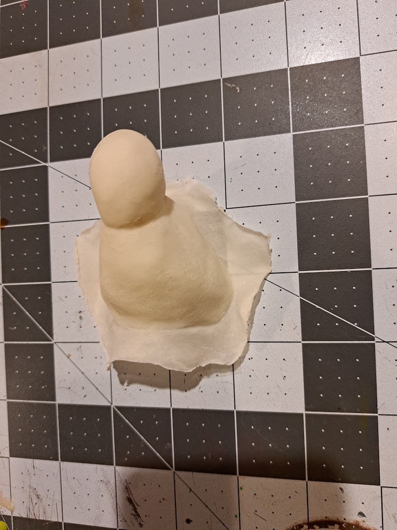 May include: A white, round, ceramic mold for making a small, round object. The mold is sitting on a black and white checkered surface.