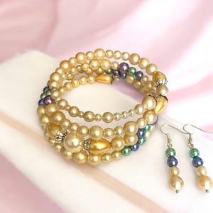 May include: A multi-strand pearl bracelet with gold and green accents, paired with matching earrings. The bracelet is made of multiple strands of pearls in a variety of sizes, with gold and green beads interspersed throughout. The earrings are simple and elegant, with a single pearl drop on each.