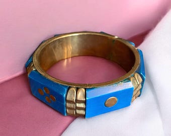Può includere: Un braccialetto blu e oro con un design geometrico. Il braccialetto è in metallo e ha una finitura lucida.