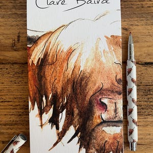 Pu&ograve; includere: Un primo piano di un dipinto ad acquerello del viso di una mucca delle Highlands. Il dipinto &egrave; su uno sfondo bianco con il testo "Clare Baird" e "MAGNETIC NOTEPAD" stampato sotto l'immagine.
