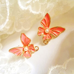 Peut inclure: Deux breloques en forme de papillon avec des contours en métal doré et des ailes en émail rose corail vif. Chaque papillon est orné d'une petite perle artificielle blanche ronde au centre et comporte un anneau de jonction à la base.