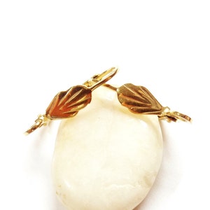 Peut inclure: Une paire de boucles d'oreilles dorées en forme de coquillage. Les boucles d'oreilles reposent sur une pierre lisse blanc cassé sur fond blanc. Les boucles d'oreilles ont un design détaillé et texturé.