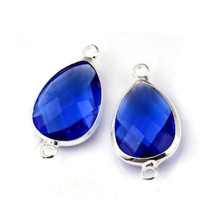 Peut inclure: Deux pendentifs en forme de goutte d'eau, en pierres précieuses bleues à facettes, avec des montures en métal argenté. Chaque pendentif comporte une boucle en haut et en bas pour l'attacher à une chaîne ou à un autre composant de bijouterie. Les pierres sont d'un bleu profond et vibrant.
