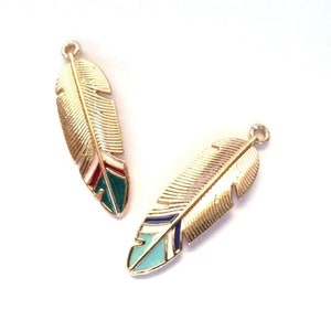 Peut inclure: Deux breloques en forme de plumes dorées avec des accents d'émail colorés. L'une présente de l'émail rouge, vert et blanc, tandis que l'autre a de l'émail bleu et turquoise. Chaque breloque a une petite boucle en haut pour la fixation.