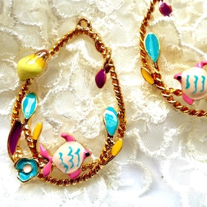 Peut inclure: Boucles d'oreilles dorées en forme de goutte d'eau sur le thème nautique. Chaque boucle d'oreille présente un motif de corde torsadée, orné de détails en émail coloré, dont un poisson rose et blanc, des feuilles turquoise et des accents jaunes.