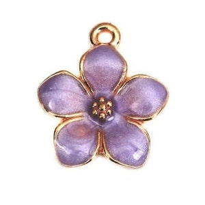 Peut inclure: Un charm en forme de fleur avec cinq pétales lavande et violets, bordés d'or. Le centre de la fleur présente un groupe de petits détails dorés. Une petite boucle dorée est située en haut pour l'attache.