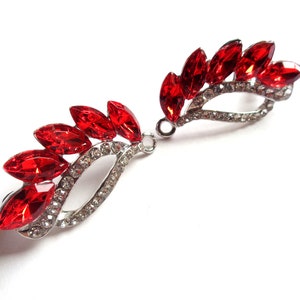 Peut inclure: Deux barrettes à cheveux argentées en forme de feuilles, ornées de pierres précieuses rouges vives, de taille marquise. Les barrettes sont ornées de petits cristaux transparents, créant un effet scintillant. Le design est symétrique et élégant.