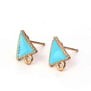 Pode incluir: Um par de brincos de pino com formato triangular e centro em esmalte turquesa brilhante. As bordas possuem uma textura de contas em tom dourado metálico e cada brinco inclui um pequeno elo circular na parte inferior para pendurar.