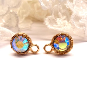 Peut inclure: Une paire de petites boucles d'oreilles à clous iridescentes. Chaque boucle d'oreille présente un cristal rond multicolore serti dans une lunette dorée ornée. Les boucles d'oreilles ont une petite boucle pour l'attache.