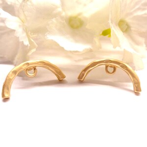 Peut inclure: Deux apprêts de bijoux dorés et incurvés avec une texture martelée. Chaque apprêt comporte une petite boucle au centre pour l'attache à d'autres composants de bijoux. Les apprêts sont posés sur un fond flou et doux.