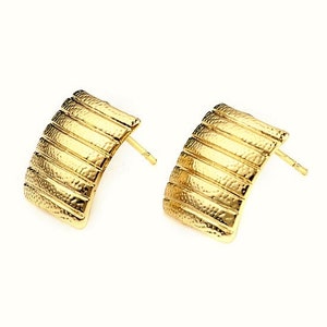 Könnte beinhalten: Ein Paar goldfarbene Ohrstecker. Jeder Ohrring hat eine gebogene, rechteckige Form mit horizontalen Rillen und einer strukturierten Oberfläche. Die Ohrringe sind vor einem weißen Hintergrund.