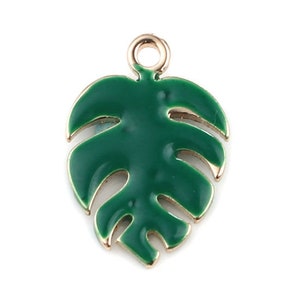 Könnte beinhalten: Ein grüner Emaille-Blatt-Anhänger mit goldfarbener Umrandung und einer Schlaufe zum Befestigen an Schmuck. Der Anhänger hat die Form eines tropischen Monstera-Blattes.