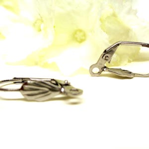 Peut inclure: Deux fermoirs de boucles d'oreilles à levier argentés. L'un est net, montrant un motif de feuille détaillé. L'autre est légèrement flou. Les fermoirs sont posés sur un fond doux et flou, suggérant un thème de fabrication de bijoux.