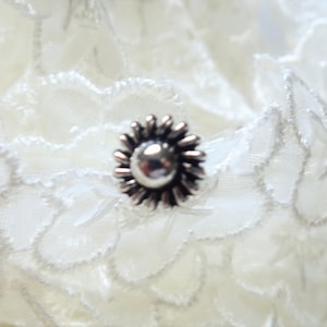 Peut inclure: Un anneau de nez en argent en forme de fleur avec un petit centre rond.