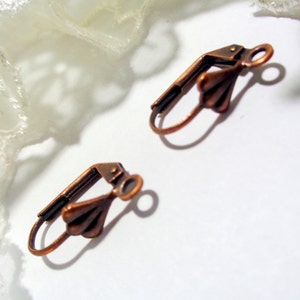 Op de afbeelding: Twee koperkleurige oorhaken met een decoratief waaiervormig ontwerp aan de bovenkant.