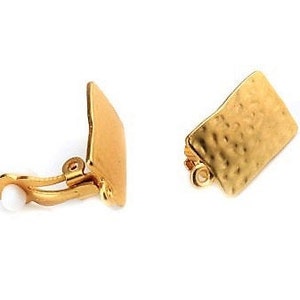 Può includere: Due orecchini a clip color oro. Ogni orecchino presenta un design rettangolare strutturato. Un orecchino è aperto, rivelando il meccanismo a clip e una piccola perla bianca. L'altro orecchino è chiuso.