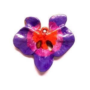 Peut inclure: Pendentif artisanal en forme de fleur stylisée. Il présente un schéma de couleurs vives avec des teintes violettes, roses et oranges. Il comporte un trou en haut pour l'enfilage et une finition brillante.