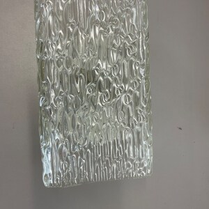 May include: A clear glass panel with a textured surface. The texture is made up of small, raised lines that create a wavy pattern.