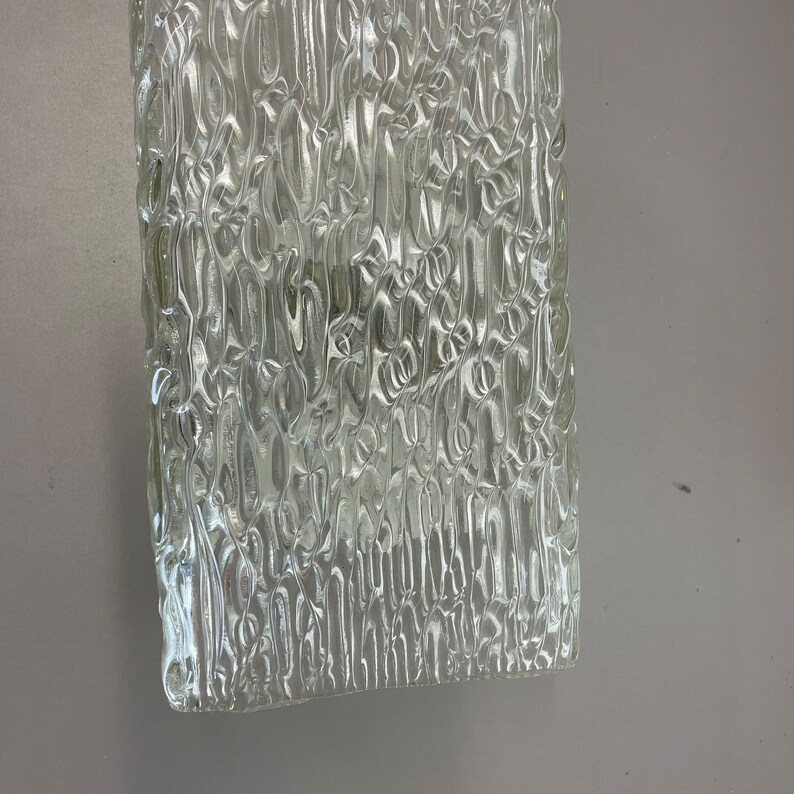 May include: A clear glass panel with a textured surface. The texture is made up of small, raised lines that create a wavy pattern.