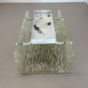May include: A clear glass ceiling light fixture with a white metal back plate and wiring. The glass has a textured, ribbed design.