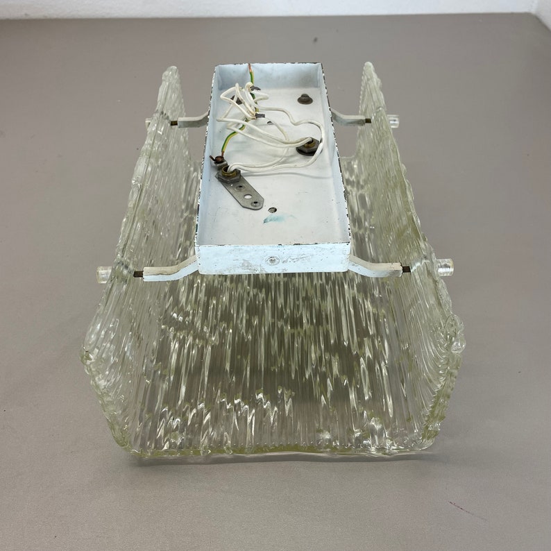 May include: A clear glass ceiling light fixture with a white metal back plate and wiring. The glass has a textured, ribbed design.
