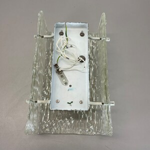 May include: A white wall sconce with a clear glass shade. The sconce has a white electrical box with wires attached to it.