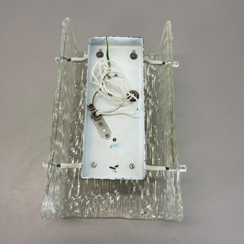 May include: A white wall sconce with a clear glass shade. The sconce has a white electrical box with wires attached to it.