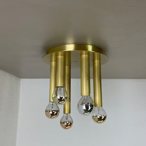 Könnte beinhalten: Eine goldene Deckenleuchte mit fünf hängenden Glühbirnen. Die Glühbirnen sind eine Mischung aus Klarglas und Kupfer.