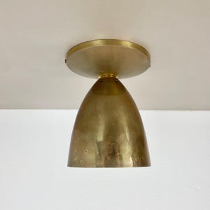 Könnte beinhalten: Eine goldene Deckenleuchte mit einer runden, flachen Oberseite und einem glockenförmigen Boden.