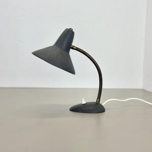 Könnte beinhalten: Eine graue Metall-Tischlampe mit flexiblem Arm und einem grauen Metallschirm. Die Lampe hat einen weißen Schalter an der Basis.