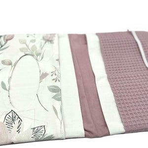 K&ouml;nnte beinhalten: Ein rosa-wei&szlig;er Stofforganizer mit mehreren Taschen und einem Blumenmuster. Der Organizer ist aus weichem, strukturiertem Stoff gefertigt und hat einen wei&szlig;en Hintergrund mit einem Blumendesign in Rosa-, Gr&uuml;n- und Graut&ouml;nen.