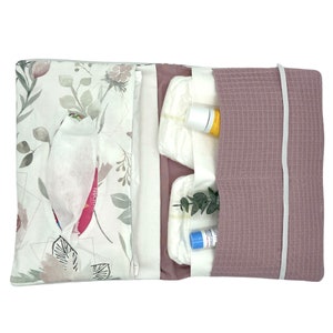 K&ouml;nnte beinhalten: Eine Wickeltasche mit floralem Druck in Rosa und Wei&szlig; mit Rei&szlig;verschluss. Die Tasche ist ge&ouml;ffnet und enth&auml;lt Windeln, Feuchtt&uuml;cher und Babylotion.