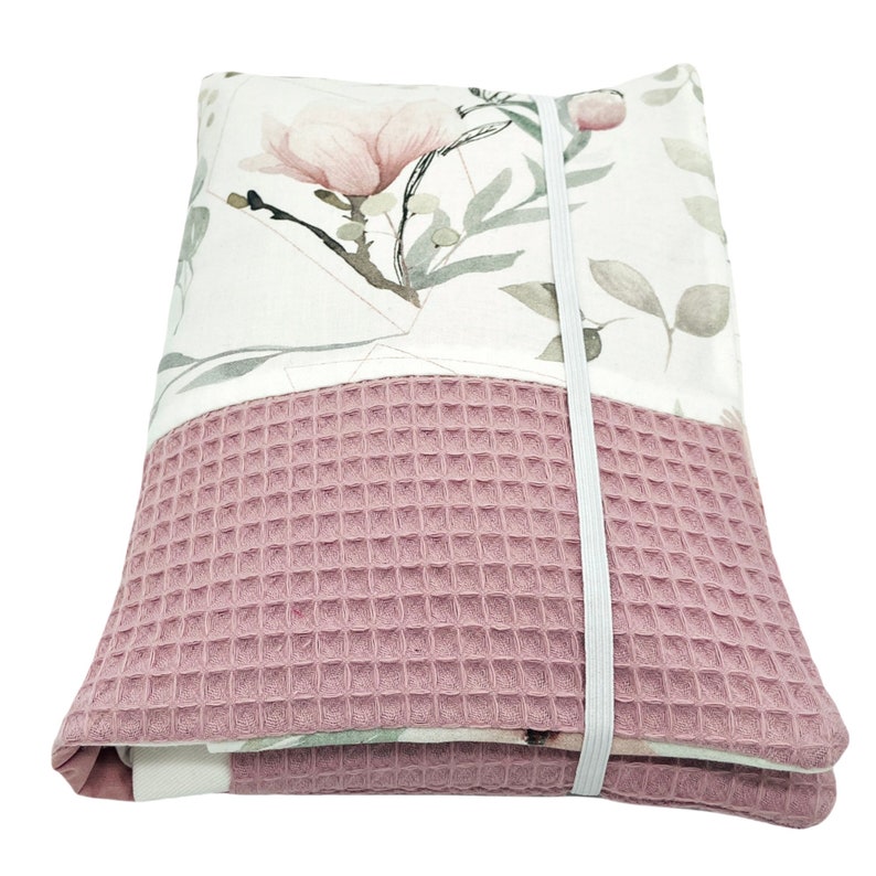 K&ouml;nnte beinhalten: Eine rosa-wei&szlig;e Stofftasche mit floralem Muster und einem waffelartigen Boden. Die Tasche hat einen wei&szlig;en elastischen Riemenverschluss.