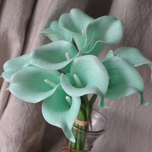 May include: A bouquet of light green calla lilies arranged in a clear glass vase. The lilies are in full bloom and have a delicate, elegant appearance.