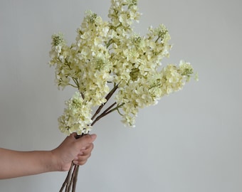 May include: A bouquet of cream-colored artificial lilac flowers with brown stems.