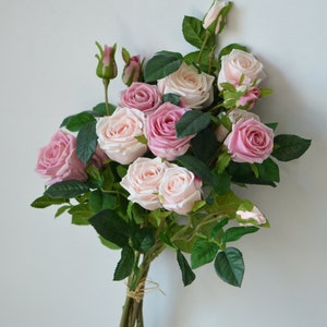 May include: A bouquet of artificial pink roses with green leaves. The roses are arranged in a cluster and tied together with twine.