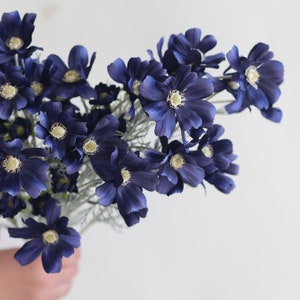 Puede incluir: Un ramo de flores artificiales de color azul oscuro con centros blancos. Las flores están dispuestas en un racimo y tienen una textura suave y aterciopelada.