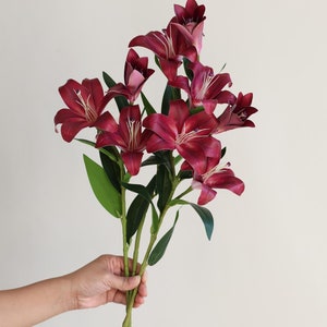 May include: A bouquet of burgundy artificial lilies with green stems and leaves.
