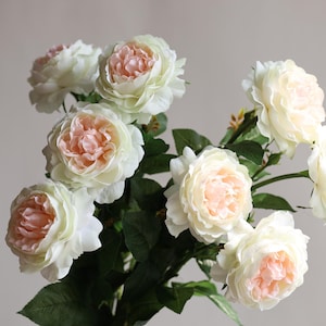 May include: A bouquet of artificial roses with white petals and pink centres. The roses are arranged in a cluster with green leaves.