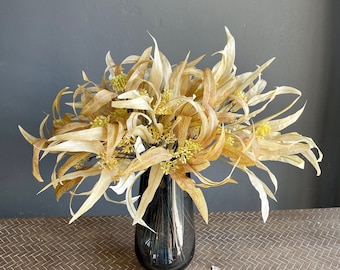 May include: A bouquet of dried, light brown, and beige flowers in a clear glass vase. The flowers are arranged in a loose, natural style.