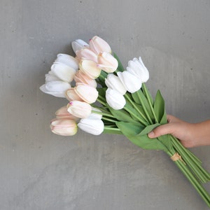 May include: A bouquet of artificial tulips in shades of white and pink. The tulips are arranged in a hand holding the stems.